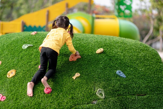 Schattig Aziatisch meisje dat plezier heeft en probeert te klimmen op kunstmatige rotsblokken op de speelplaats van het schoolplein Klein meisje dat op de rotswand klimt Hand-oogcoördinatie Vaardighedenontwikkeling