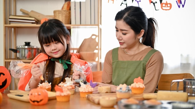 Schattig Aziatisch meisje decoreert en maakt een cupcake voor haar Halloween-feestje met haar moeder