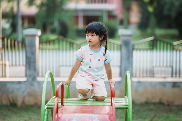 Schattig aziatisch meisje glimlach spelen op school of kleuterschool of speeltuin Gezonde zomeractiviteit voor kinderen Klein Aziatisch meisje klimmen buiten op speelplaats Kind spelen op buitenspeeltuin