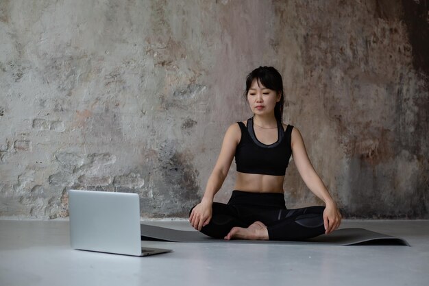 schattig Aziatisch meisje met donker lang haar in trainingssportkleding die online yoga doet met een laptop