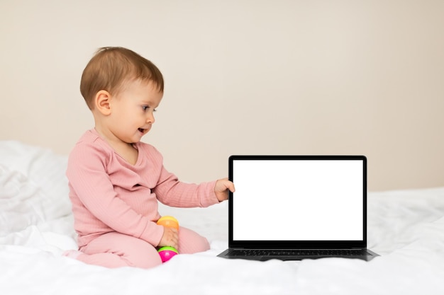 Schattig babymeisje dat naast een laptop zit met lege schermruimte voor website of