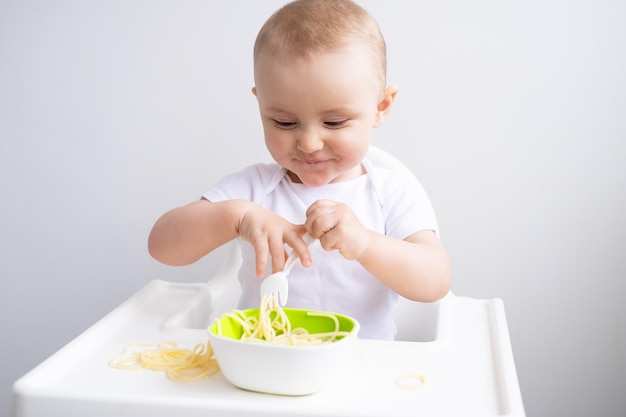 schattig babymeisje eten spaghetti pasta zittend in de kinderstoel op witte keuken