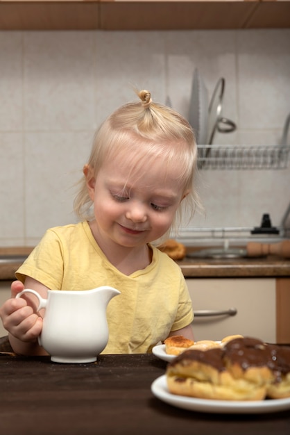 Schattig blond kind ontbijt in de keuken. Klein meisje het drinken van thee met snoep.