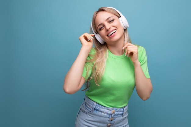 Schattig blond meisje in casual outfit luistert naar muziek op de app in grote witte koptelefoon op een blauw