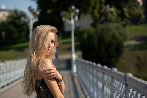 Schattig blond meisje met natuurlijke make-up en lang haar met kanten top, poserend met zonlicht. Ruimte voor tekst