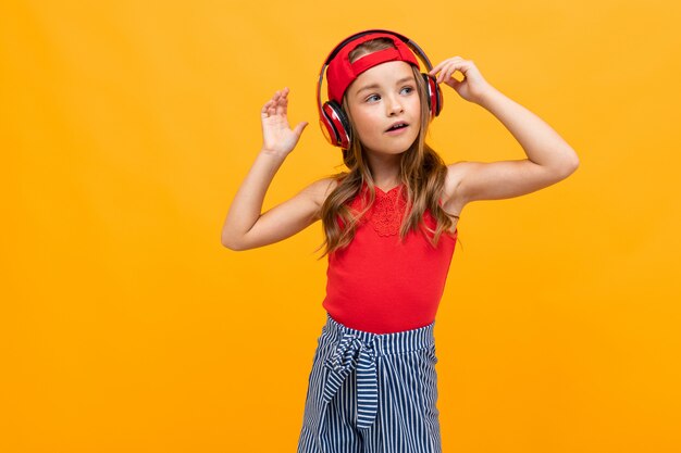 schattig charmant jong meisje in een casual look met rode koptelefoon op een gele muur