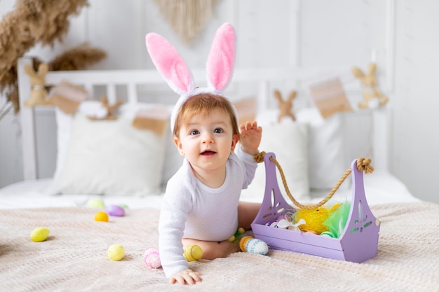 Schattig gelukkig babymeisje in konijnenoren op het bed thuis met een konijn en beschilderde eieren Pasen concept grappige paasbaby wacht op de vakantie en verheugt zich