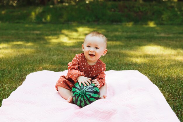 Schattig gelukkig babymeisje met een bal zit op groen gras in het park