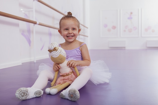 schattig gelukkig ballerina meisje lachen naar de camera, poseren met haar ballerina pop in dansstudio