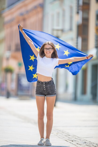 Schattig gelukkig jong meisje met de vlag van de europese unie in de straten ergens in europa.