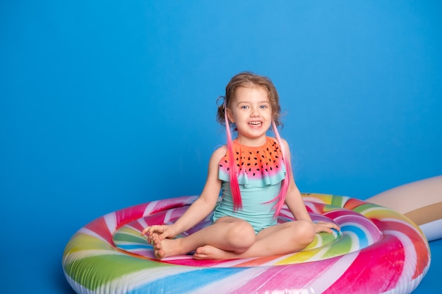 Schattig gelukkig klein meisje in zwempak glimlachend zittend op kleurrijke opblaasbare matras.