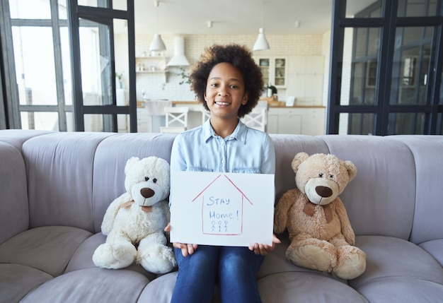 Schattig gemengd ras tienermeisje in vrijetijdskleding glimlachend naar de camera en vasthoudend thuis blijven tekenen terwijl