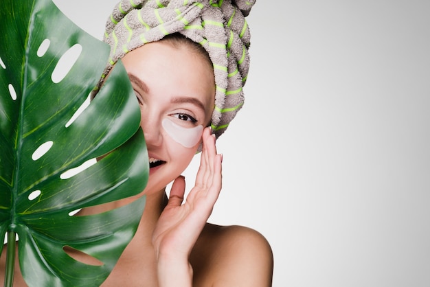 Schattig glimlachend meisje met een handdoek op haar hoofd met een groen blad, genietend van een spa, onder de ooglapjes