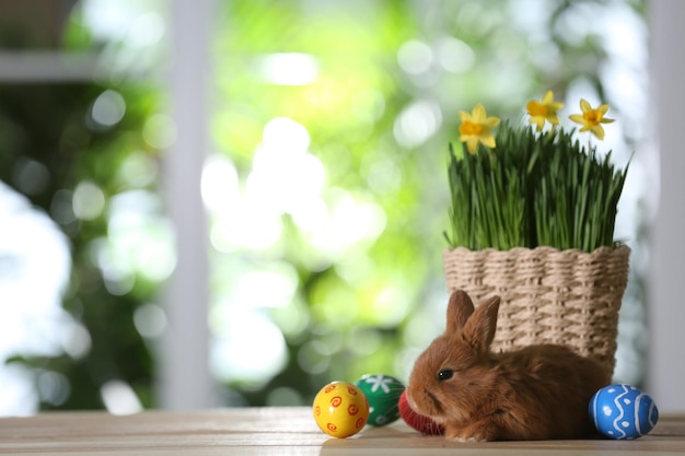 Schattig harig konijn geverfd paaseieren en bloemen op houten tafel tegen onscherpe groene achtergrond Ruimte voor tekst