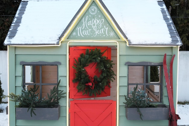 Foto schattig houten geschilderd roodgroen privé kinderspeelhuis in huistuin versierd met kerstkrans buiten in koude besneeuwde winderavond