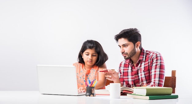 Schattig indiaas meisje met vader die thuis studeert of huiswerk maakt met laptop en boeken - online scholingsconcept