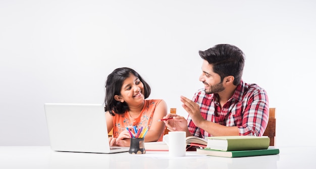 Schattig Indiaas meisje met vader die thuis studeert of huiswerk maakt met laptop en boeken - online scholingsconcept