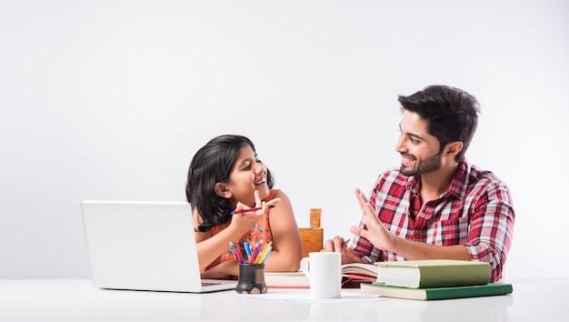 Schattig Indiaas meisje met vader die thuis studeert of huiswerk maakt met laptop en boeken - online scholingsconcept