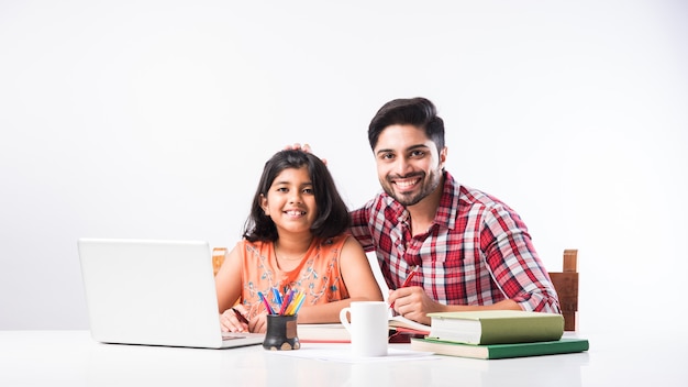 Schattig Indiaas meisje met vader die thuis studeert of huiswerk maakt met laptop en boeken - online scholingsconcept