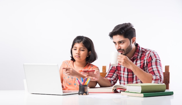 Schattig Indiaas meisje met vader die thuis studeert of huiswerk maakt met laptop en boeken - online scholingsconcept