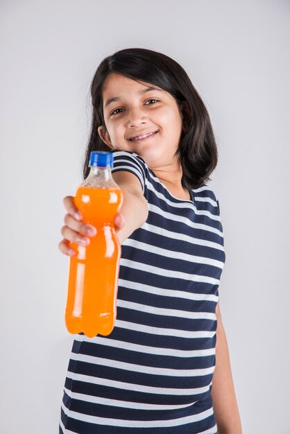 Schattig Indiaas of Aziatisch meisje met een petfles sinaasappel of mango koud drankje of vruchtensap, drinken of vasthouden terwijl ze geïsoleerd staan over blauwe of witte achtergrond.