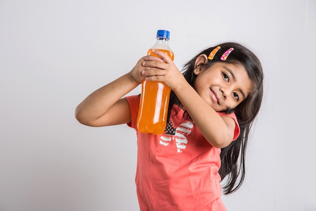 Schattig indiaas of aziatisch meisje met een petfles sinaasappel of mango koud drankje of vruchtensap, drinken of vasthouden terwijl ze geïsoleerd staan over blauwe of witte achtergrond.