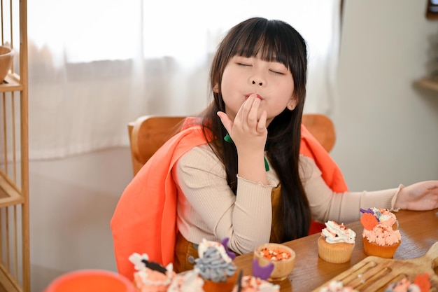 Schattig jong Aziatisch meisje geniet thuis van het eten van een pompoencupcake op een Halloween-feest