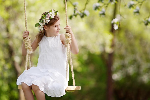 Schattig jong meisje dat plezier heeft op een schommel in een bloeiende oude appelboomtuin Zonnige dag Lente buitenactiviteiten voor kinderen