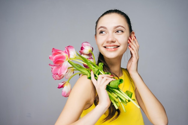 Schattig jong meisje geniet van de lente in een gele jurk met geurige roze bloemen en glimlacht