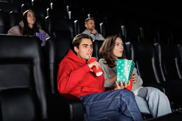 Schattig jong stel drinkt limonade en eet popcorn in de bioscoop