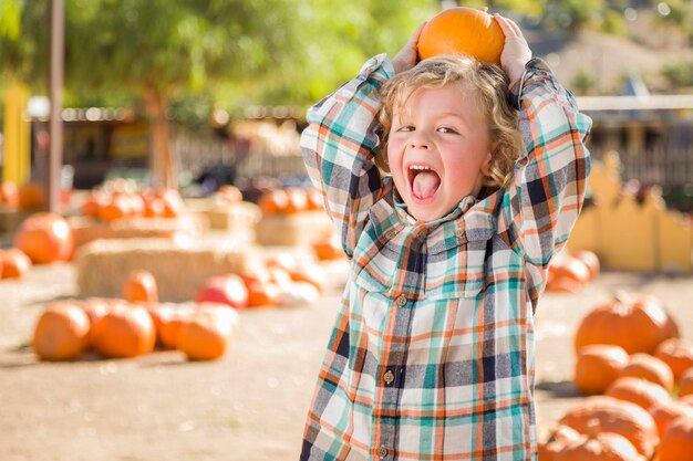 Schattig jongetje zit en houdt zijn pompoen vast in een rustieke ranchomgeving op het pompoenveld