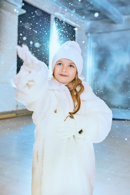 schattig Kaukasisch blond meisje in een witte ecobontjas, muts en handschoenen die in de winter kerstmis lopen