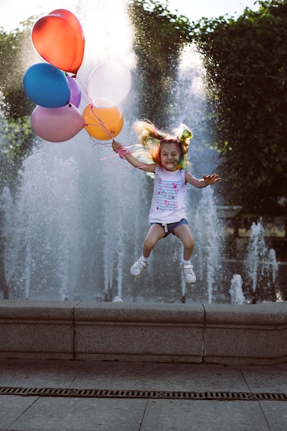 schattig Kaukasisch lachend meisje met kleurrijk geverfd haar met ballonnen die uit de fontein springen