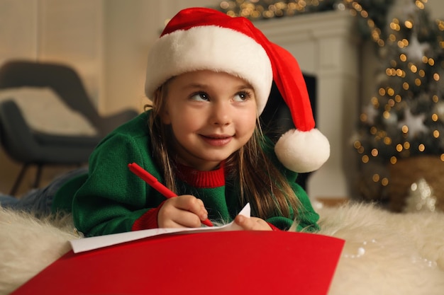 Schattig kind dat een brief schrijft aan de kerstman terwijl hij op de vloer ligt thuis kerstviering