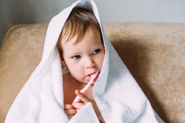 Schattig kind in grote witte handdoek, ze poetst zijn tanden met tandenborstel