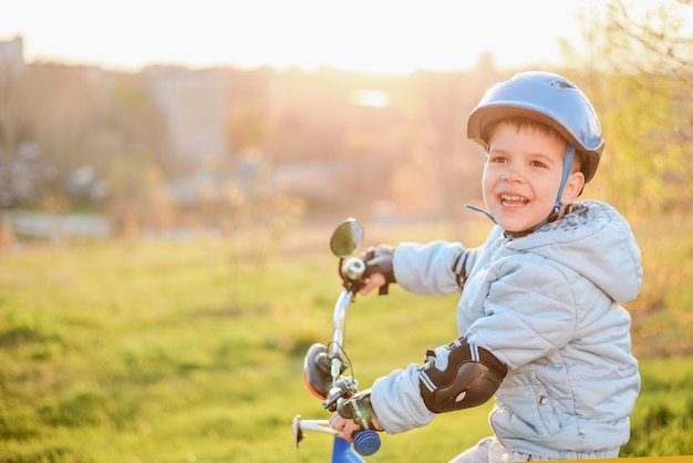 Schattig kind in helm leert en fietst op een zonnige dag bij zonsondergang