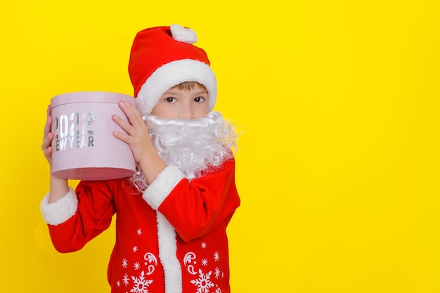 schattig kind in kerstmankleding en met baard met een roze ronde geschenkdoos in zijn handen