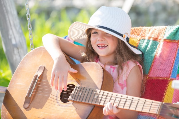 Schattig kind meisje met blond krullend haar gitaarspelen op natuur achtergrond gelukkig schattig tiener meisje swingen en plezier gezonde zomervakantie activiteit kinderen muziek en liedjes