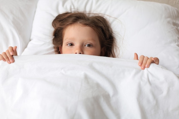 Schattig kind meisje werd wakker en ligt in het bed.