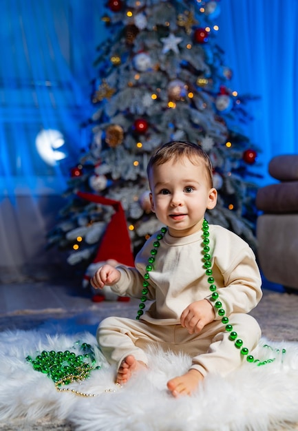 Schattig kind met kerstboom Gelukkig baby zitten in de buurt van een dennenboom en houden een kerst ornament en glimlachen Prettige kerstdagen en fijne feestdagen