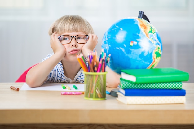 Schattig kind saai op de les. Het kind wil geen huiswerk of klaswerk maken. Ongelukkige schooljongen.