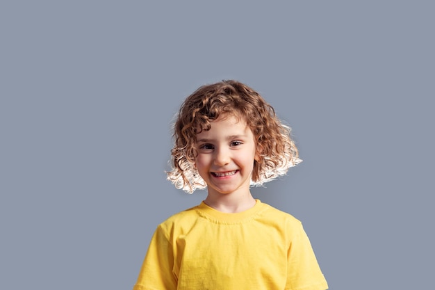 Schattig kind van 5 jaar in gele t-shirt poseren op grijs