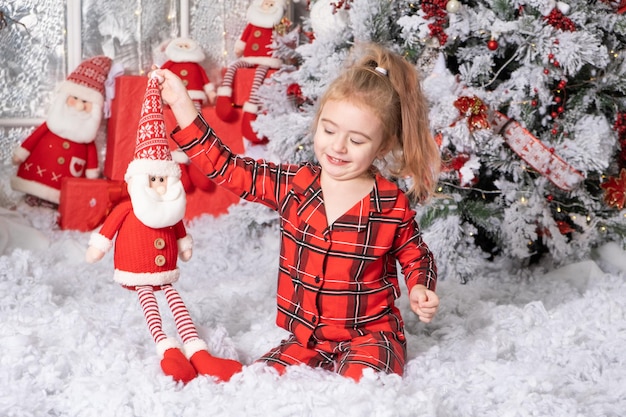 Schattig klein babymeisje dat speelt met het speelgoed van de kerstman in een met kerst versierde kamer, vrolijk kerstconcept