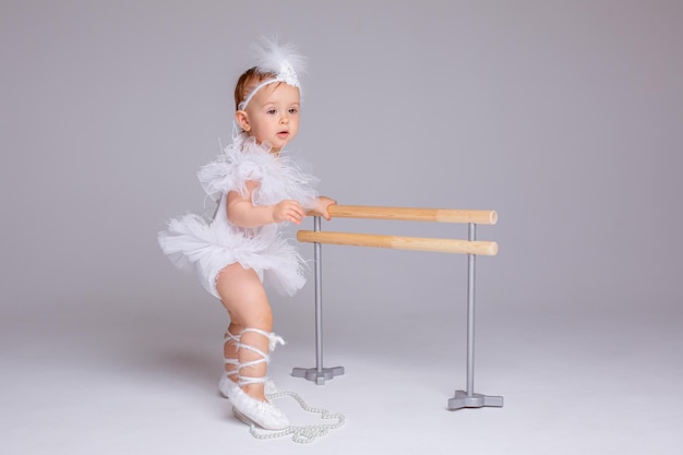 Schattig klein babymeisje in een ballerinakostuum met een balletmachine op een witte achtergrond