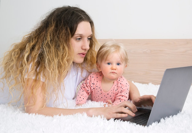 Schattig klein babymeisje met laptop in ouder slaapkamer.