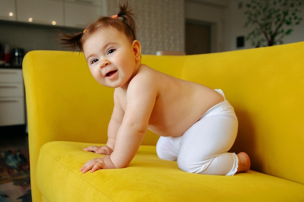 Schattig klein babymeisje op de gele bank die eerste stappen thuis maakt, gelukkig peutersportret, vreugde van c...