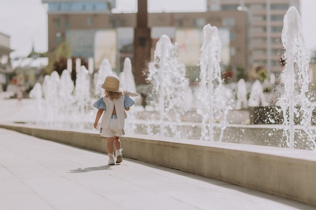 schattig klein blond meisje in blauwe jurk en strohoed spelen in de buurt van fontein met pluche konijntje, kaart