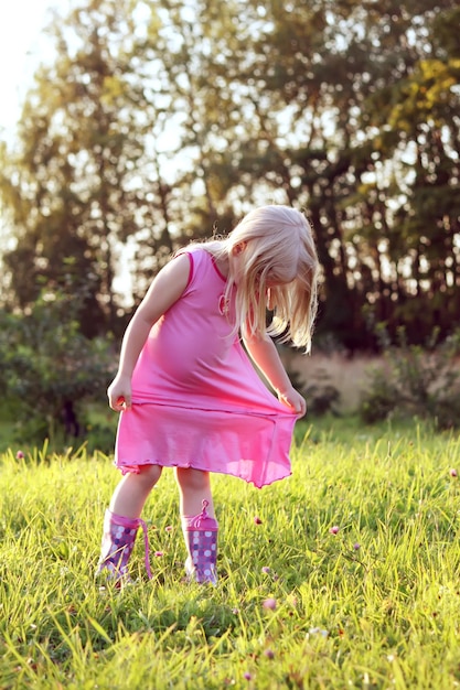 Schattig klein blond meisje in een roze jurk spelen in een weide in zonnige zomerdag