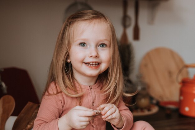 schattig klein blond meisje in roze pyjama koekjes eten in de keuken gezonde snack voor kinderen