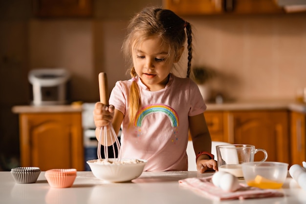 Schattig klein blond meisje kookt deeg in de keuken thuis